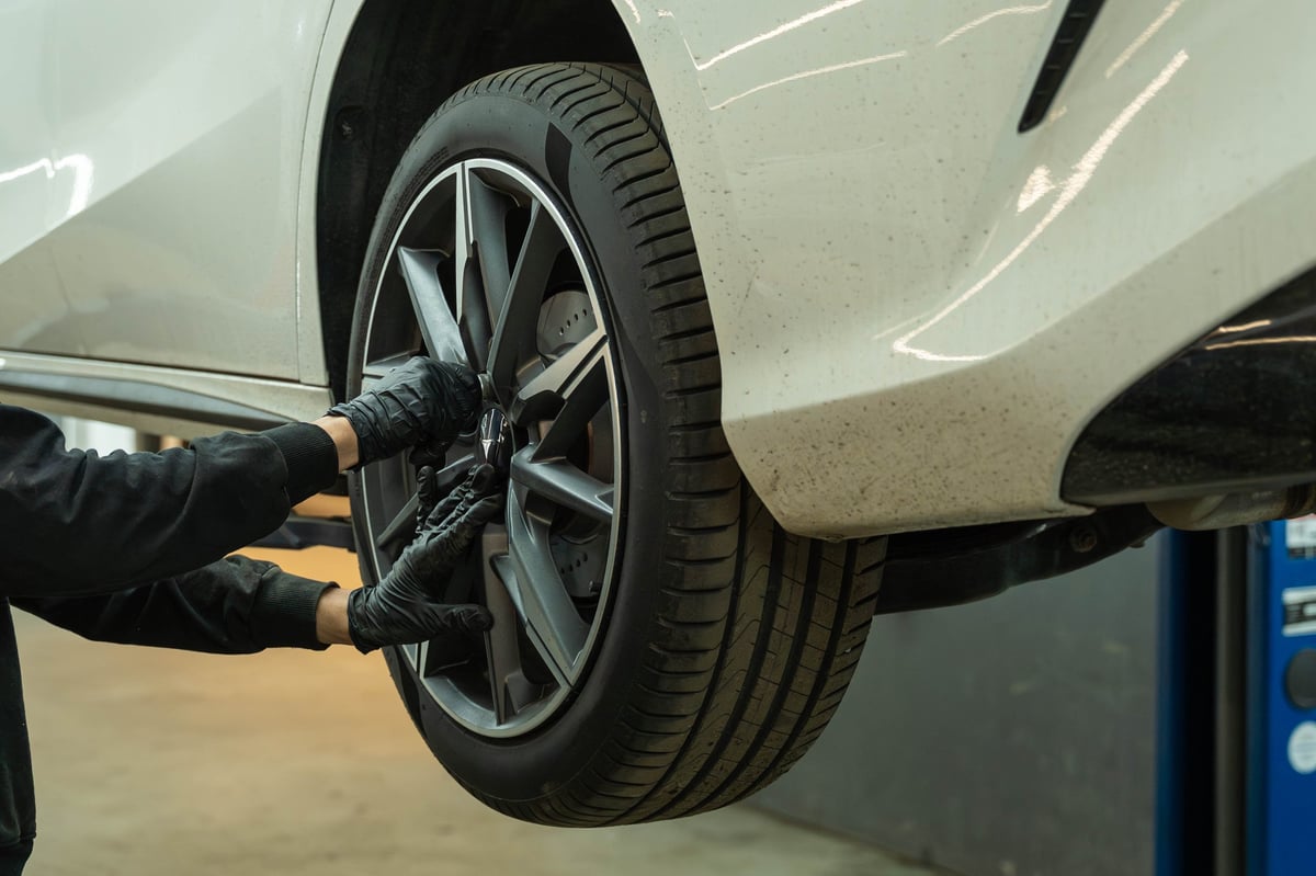 Gloved hands working on a car wheel while the vehicle is raised on a workshop lift